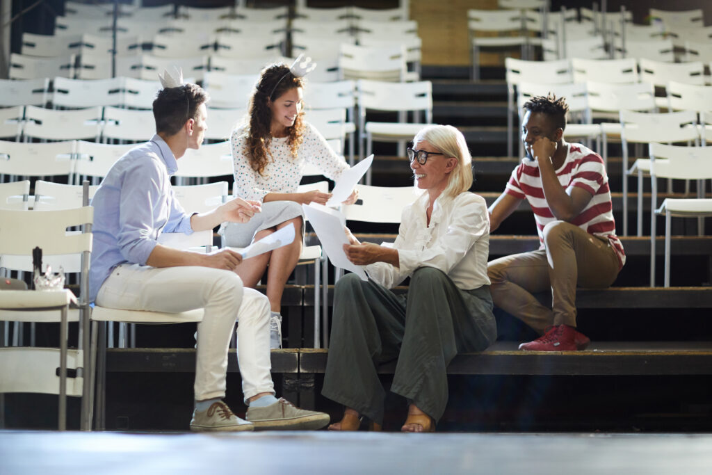 Group of young people and their coach reading papers with screenplay during stage repetition